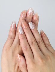 Hand model wearing short pink square press-on nails with shimmering gold glitter tips and thin gold line accents