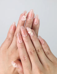 Hand model wearing pink oval press-on nails with raised floral details and delicate pearl accents
