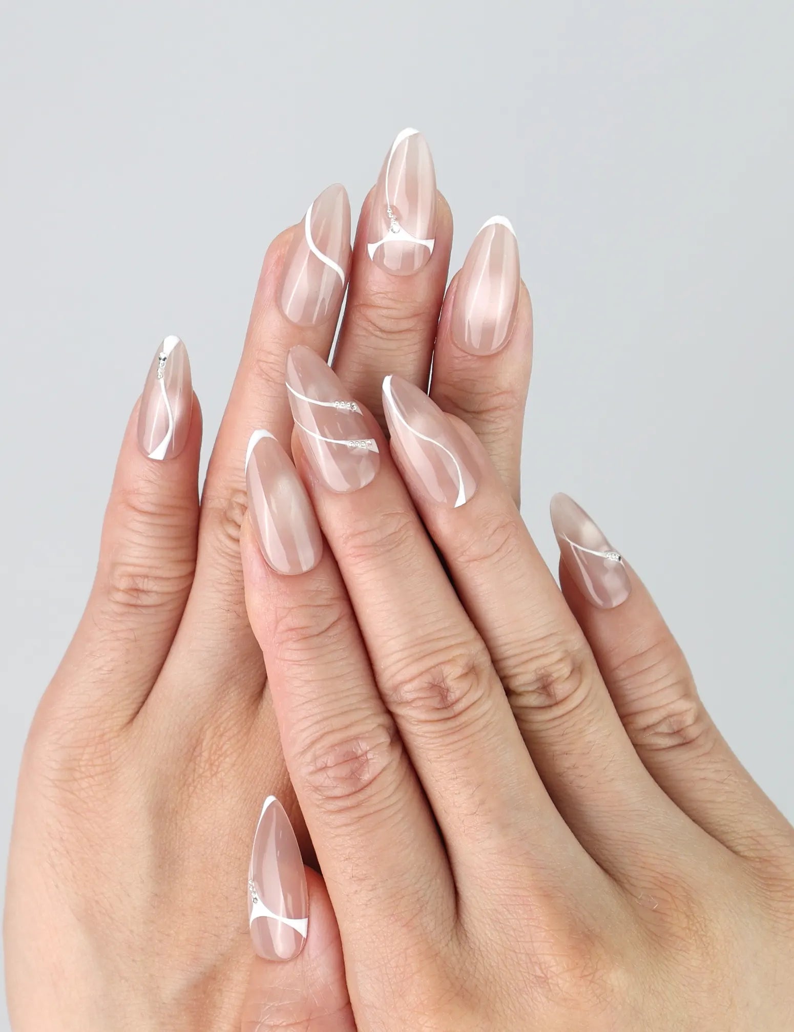 Hand model wearing taupe press-on nails with abstract white swirls and metallic gold accents