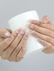 Hand holding a cup, showcasing Naillover’s taupe press-on nails with modern swirl art and subtle gold touches