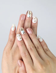 Hand model wearing short pink square press-on nails with fine white floral patterns and subtle shimmer finish