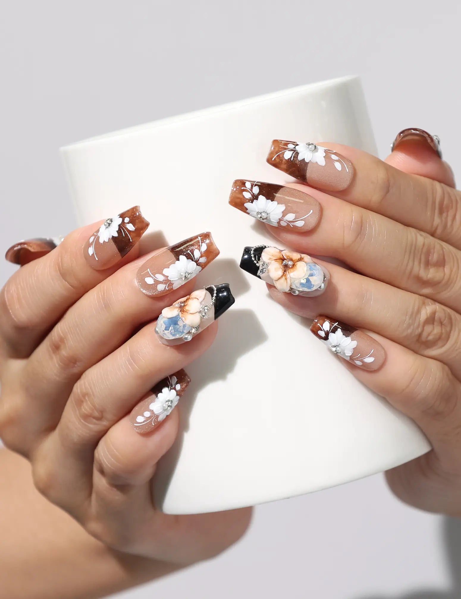 Hand holding a coffee cup while wearing Amber Bloom handmade Singapore press on nails with floral and rhinestone details