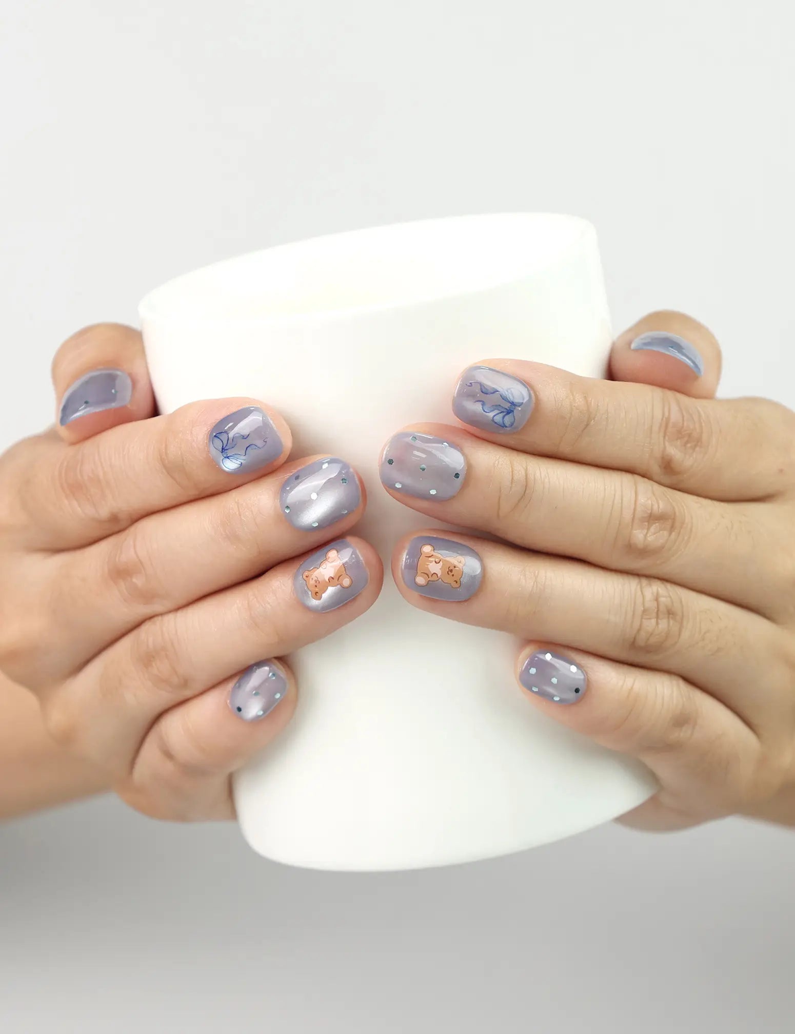 Model holding cup while wearing Aqua Flash Singapore press on nails in vibrant blue, ribbon, and bear design