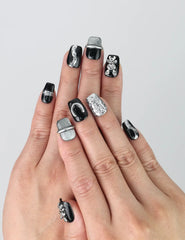 Hand model wearing glossy black short coffin nails with metallic 3D bunny accents and a sleek finish
