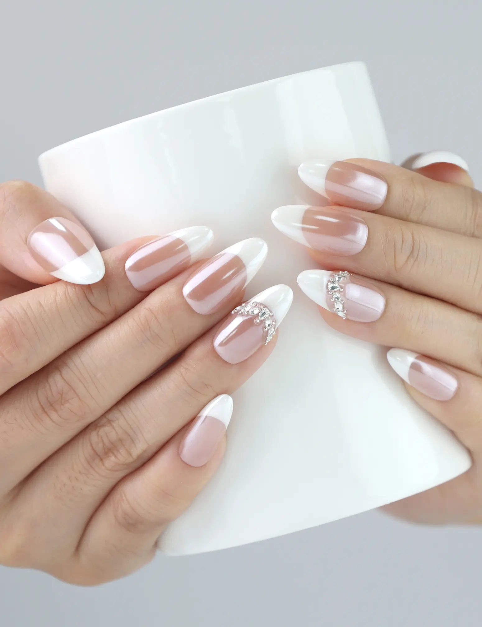 Hand holding a cup, showcasing Naillover’s pink ombré almond nails with dainty rhinestones