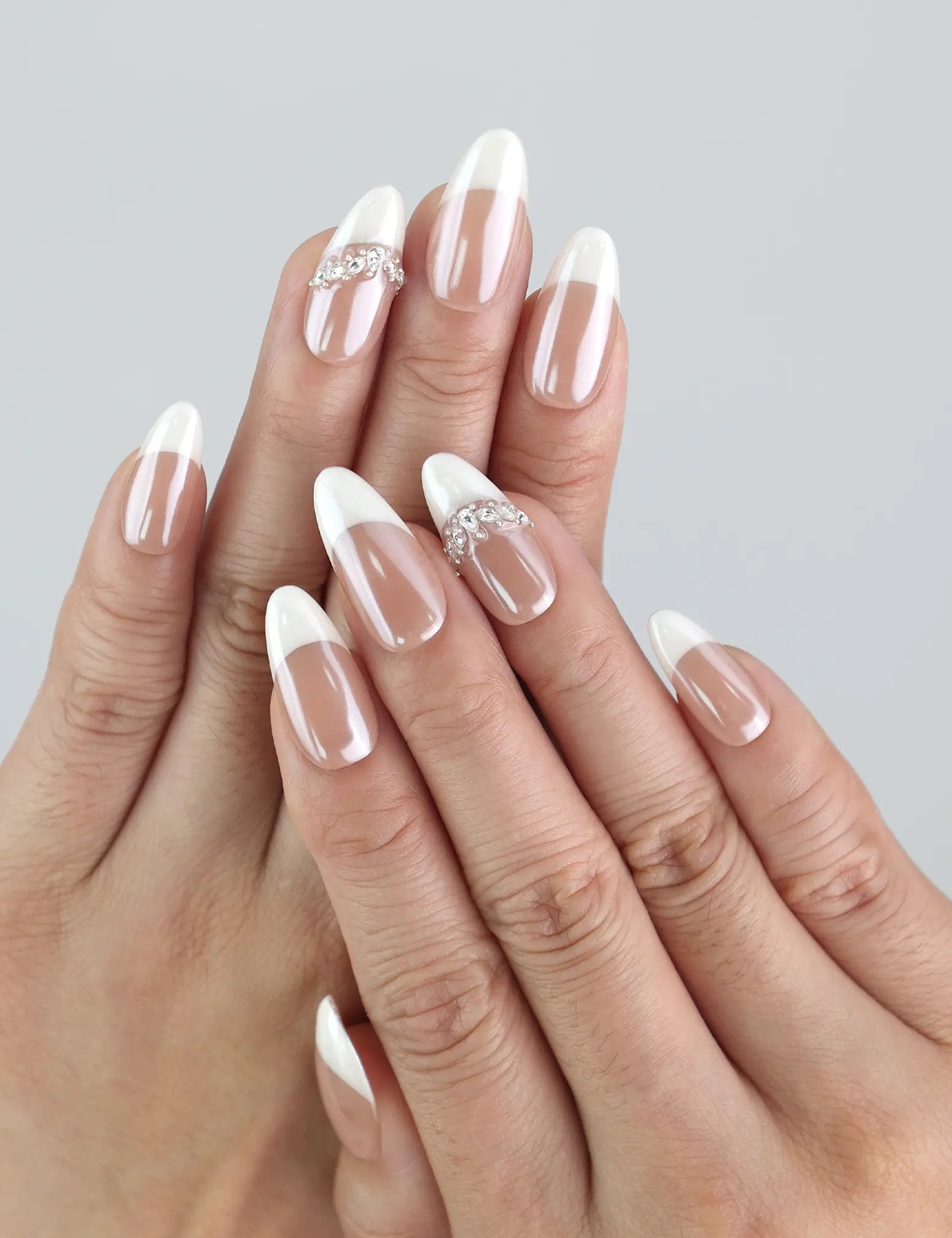 Hand model wearing almond press-on nails with soft pink-to-white gradient and sparkling rhinestone accents