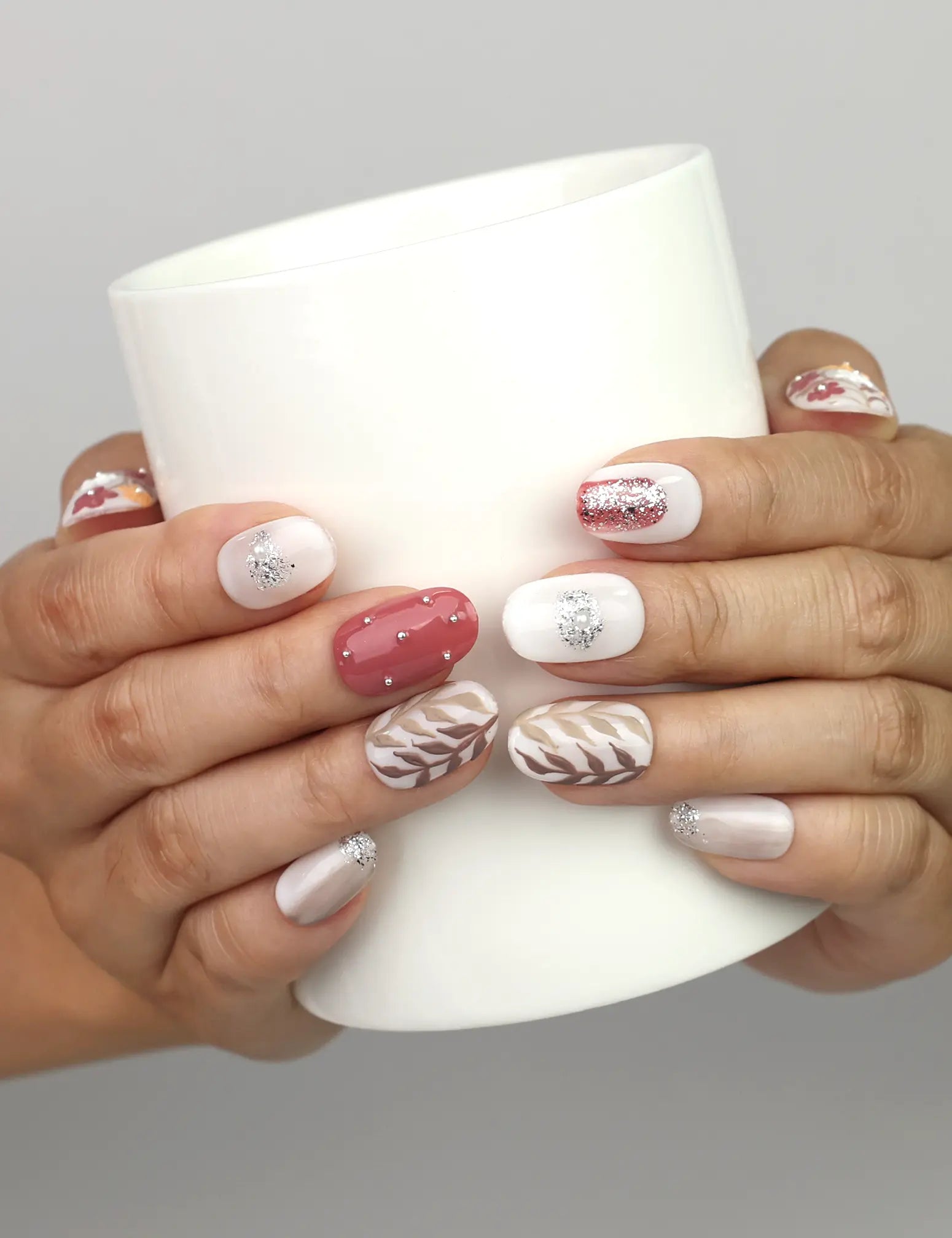 Hand holding a cup while wearing Naillover Autumn Floral Sparkle handmade press on nails with autumn leaf and floral sparkle design.