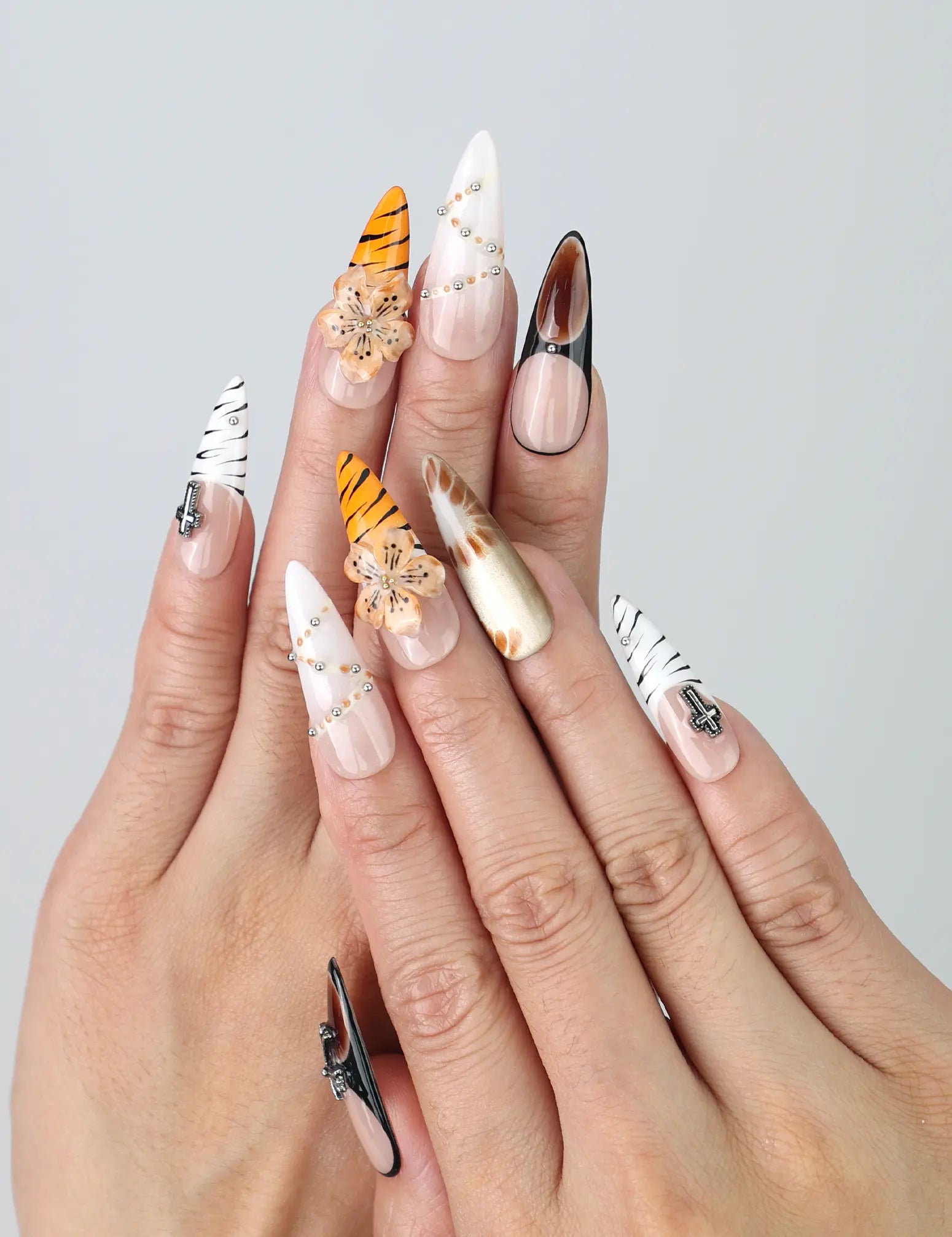 Hand model showing stiletto-shaped press-on nails in warm earth tones with bold tiger stripe patterns and floral 3D accents