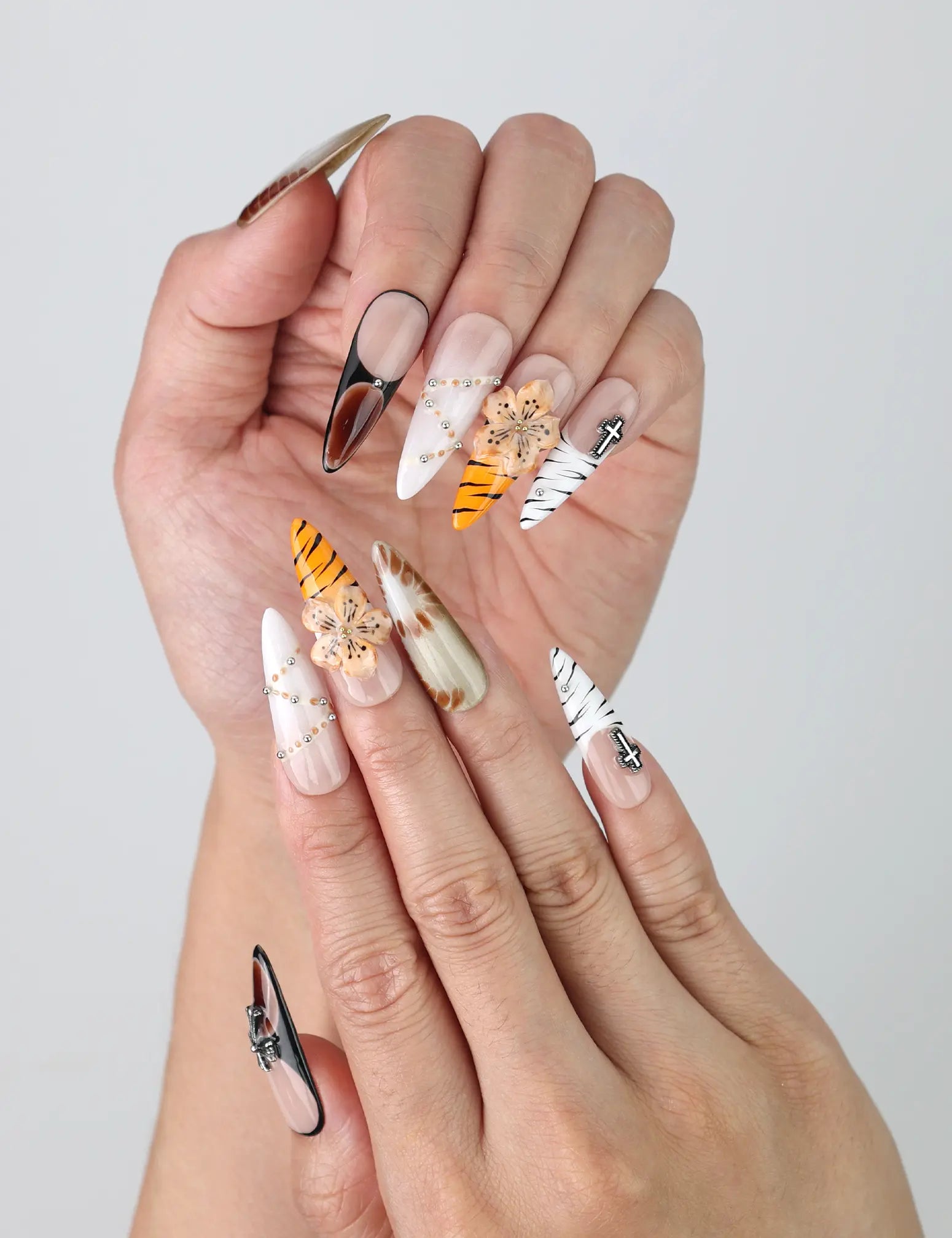 Close-up of handmade stiletto nails with natural color palette, crystal embellishments, and intricate flower nail art