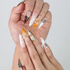 Close-up of handmade stiletto nails with natural color palette, crystal embellishments, and intricate flower nail art