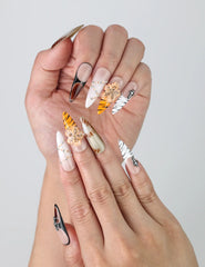 Close-up of handmade stiletto nails with natural color palette, crystal embellishments, and intricate flower nail art