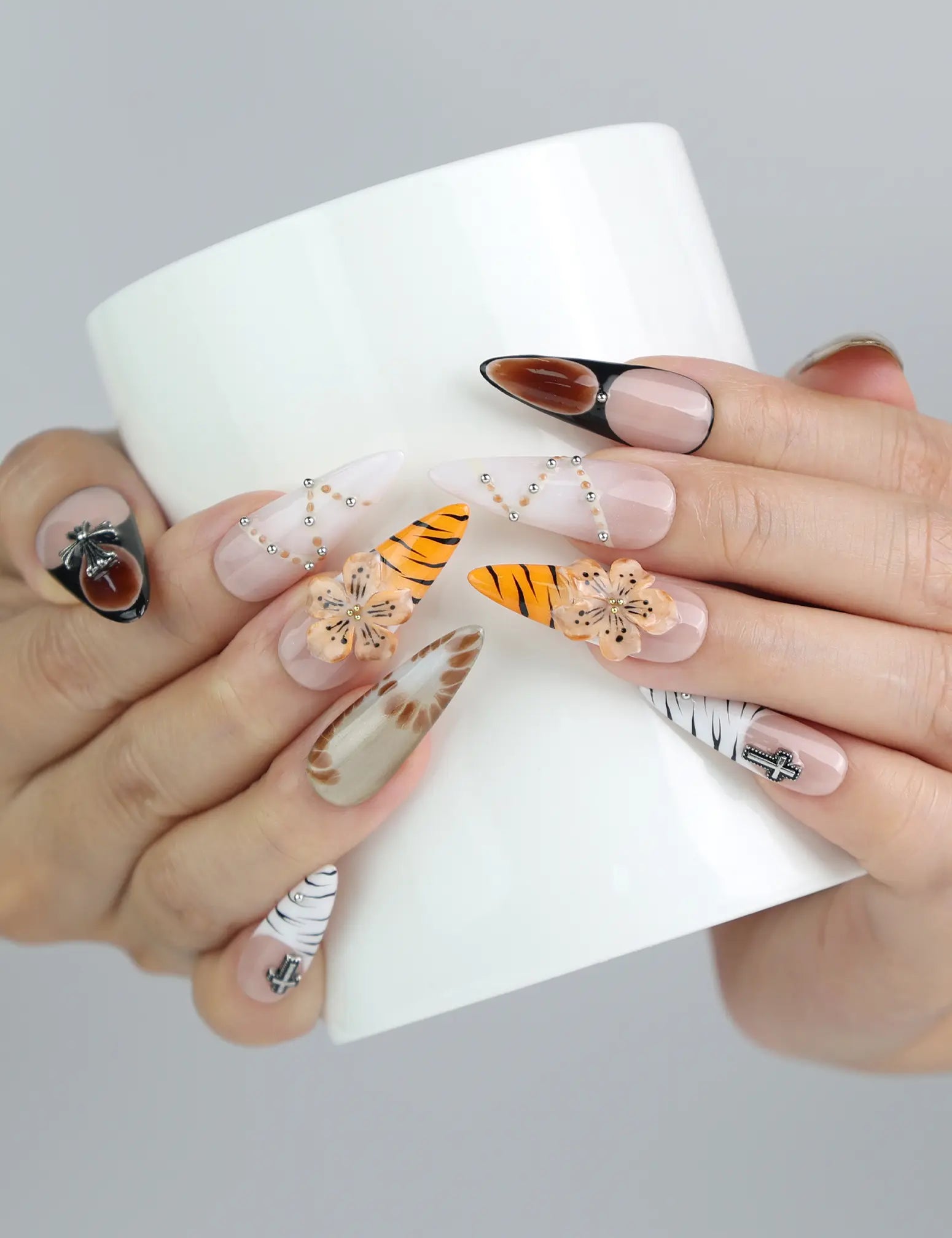 Hand holding a cup, wearing Naillover stiletto press-on nails in earthy brown hues with tiger stripes and 3D floral crystals