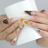 Hand holding a cup, wearing Naillover stiletto press-on nails in earthy brown hues with tiger stripes and 3D floral crystals