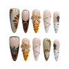Product display of handmade stiletto press-on nails in neutral tones with tiger stripes, crystals, and dimensional flowers