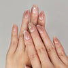 Hand wearing Naillover Autumn Whisper handmade press on nails in nude-to-brown ombre with delicate gold foil accents.