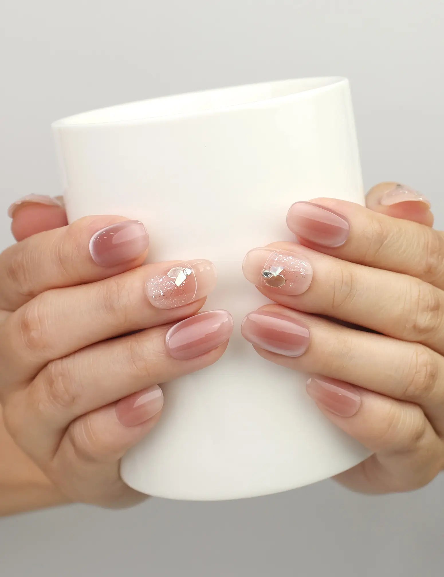 Hand holding a cup while wearing Naillover Autumn Whisper Singapore press on nails in nude brown ombre with gold foil leaf accents.