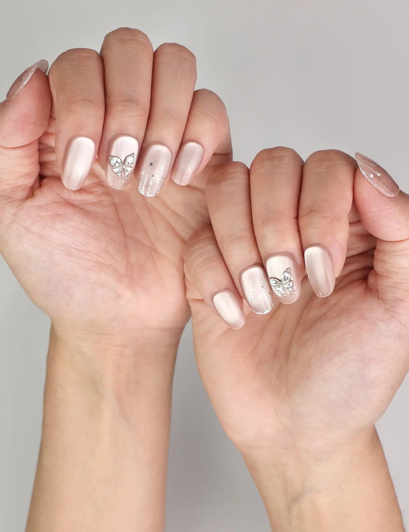 Naillover Beige Elegance trendy nails styled on hand, showcasing handmade cat eye shimmer nails with silver butterfly charm details.