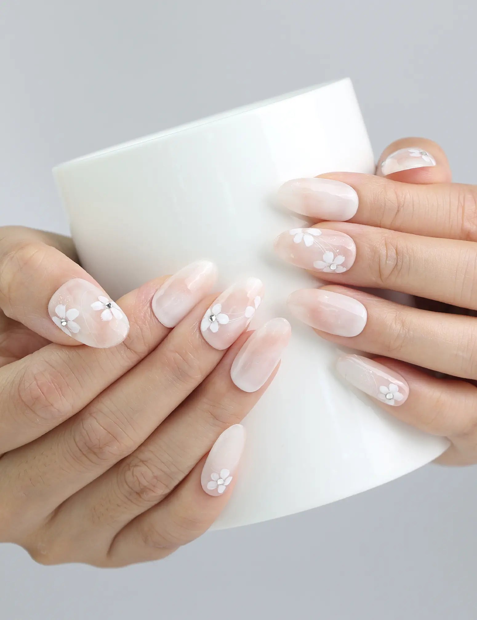 Holding a cup while wearing Singapore handmade sheer press on nails with dainty pink and white floral details by Naillover
