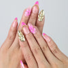 Hand model wearing handmade pink press-on nails with gold shimmer, 3D pink flowers, pearl accents, and tiny stars