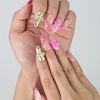 Close-up of Naillover pink nails with golden sparkle base, raised floral details, and elegant pearl and star embellishments