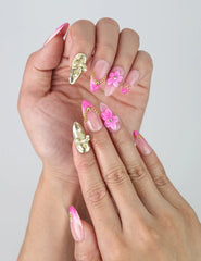 Close-up of Naillover pink nails with golden sparkle base, raised floral details, and elegant pearl and star embellishments