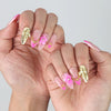 Side view of short pink press-on nails with glistening finish, delicate flower art, and mixed pearl-star charm arrangement