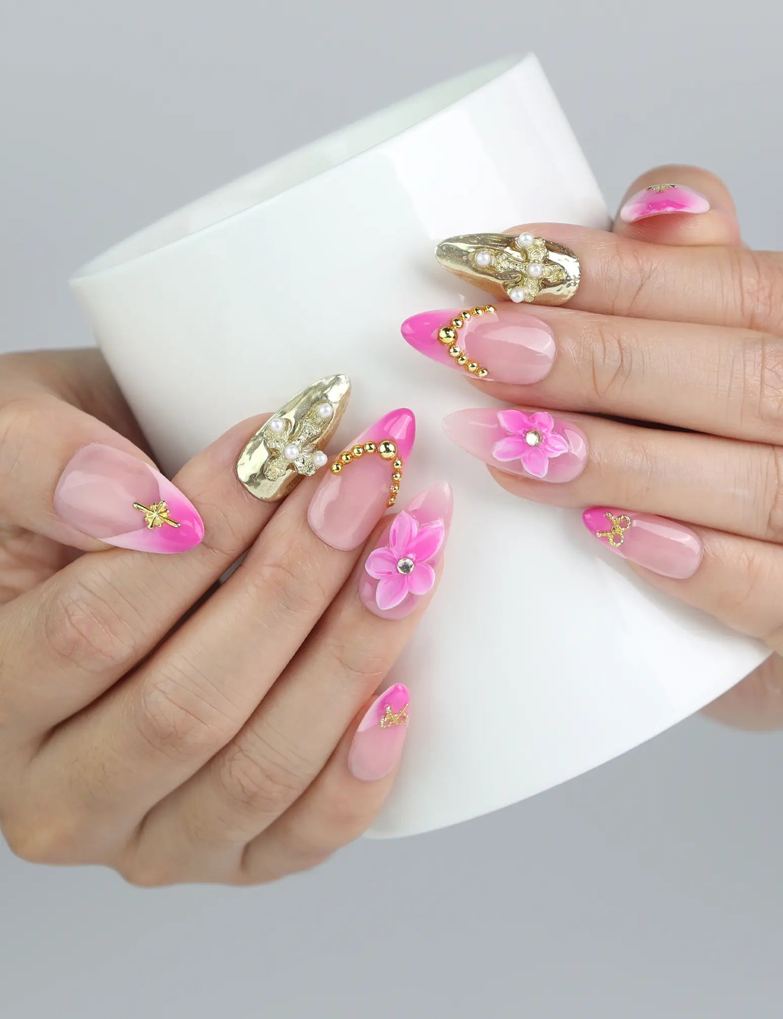 Hand holding a cup while showcasing Naillover’s pink press-on nails with 3D flowers, gold shimmer, and decorative pearls