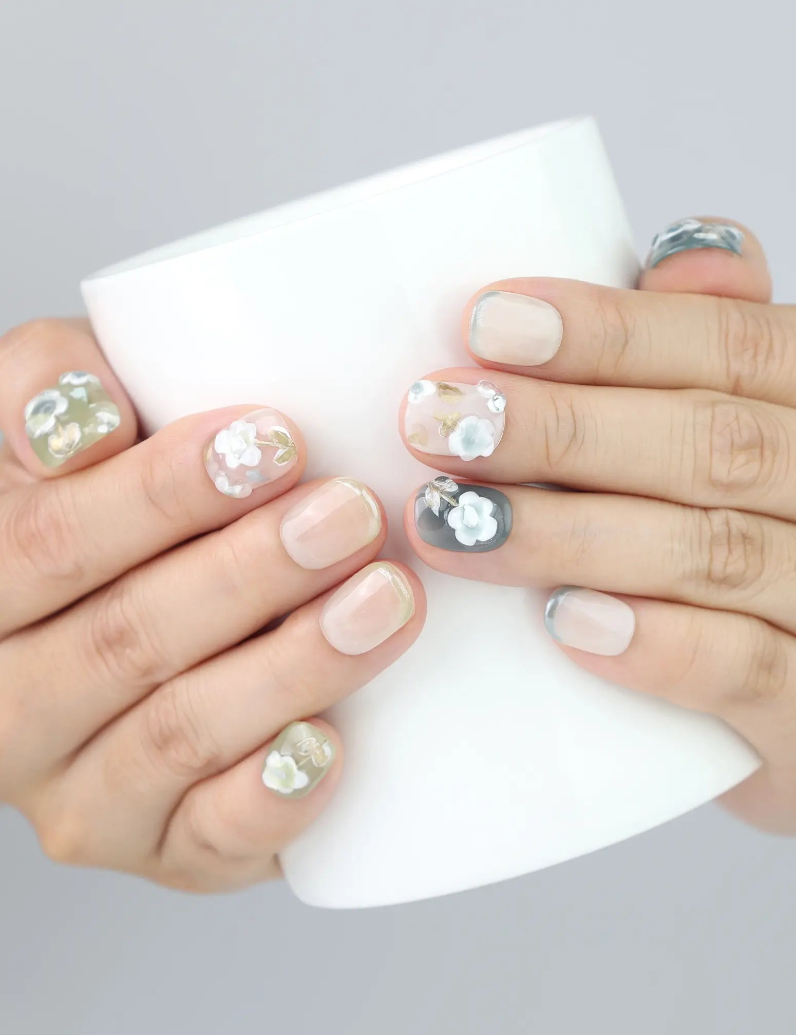 Holding a cup while wearing Singapore handmade press on nails with white 3D flowers and olive French fade base by Naillover