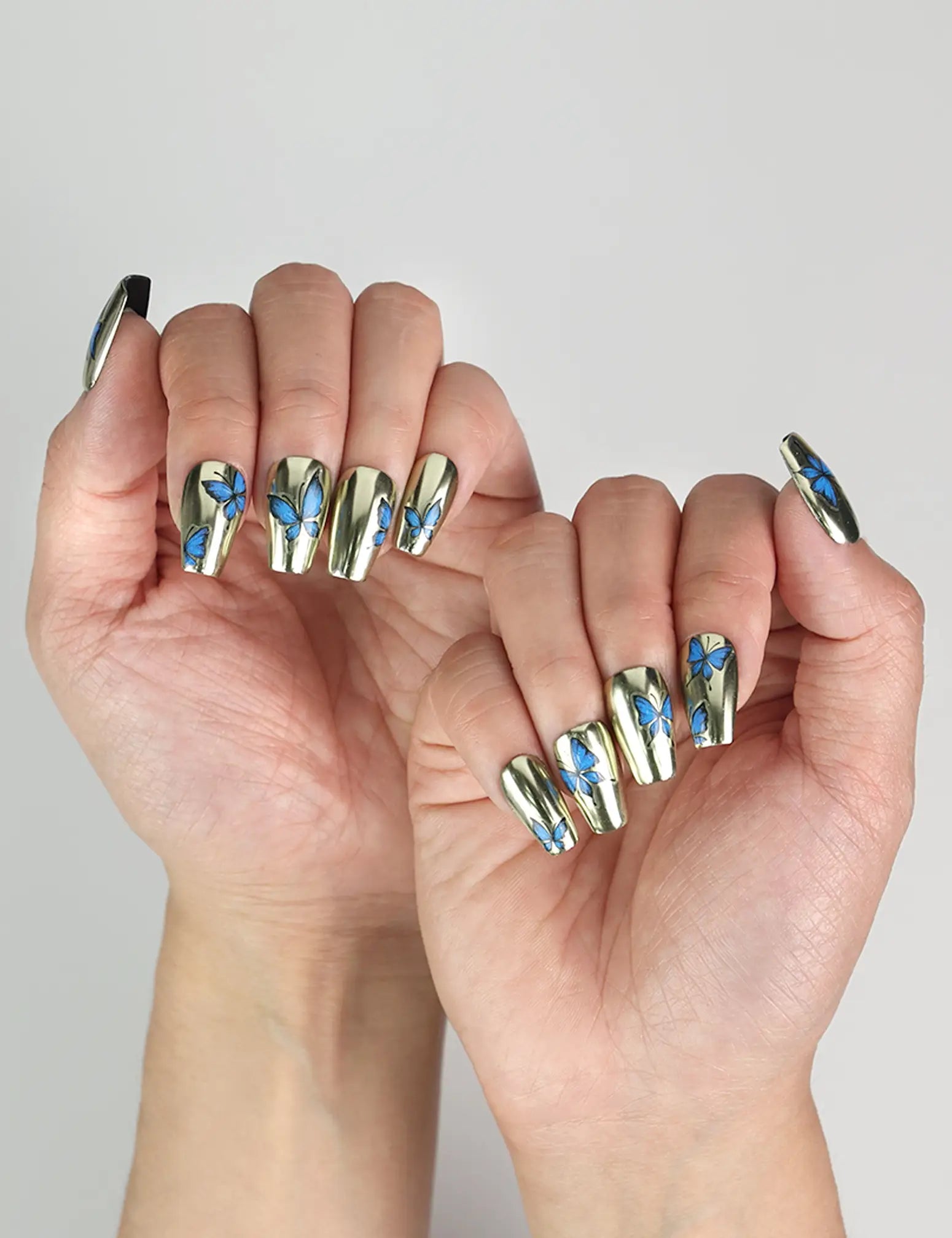 Model hand showcasing Blue Aura Singapore press on nails, featuring golden sheen and detailed butterfly accents.