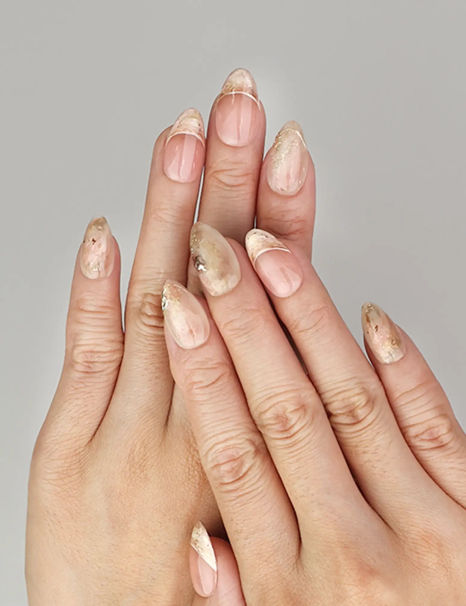 Hand wearing Naillover Blush Amber Grace handmade press on nails in peach and beige marble with chic gold details.