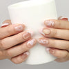 Hand holding a cup while wearing Naillover Blush Latte handmade press on nails in nude ombre with metallic stripe accents.