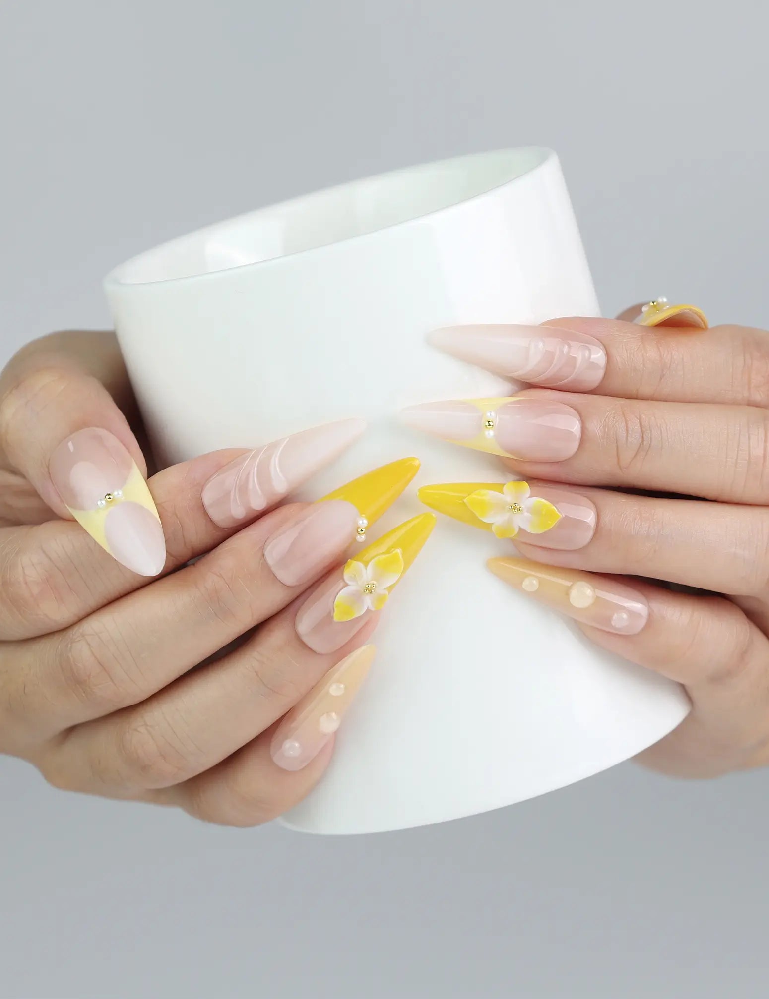 Hand holding a cup while wearing Naillover’s yellow and galaxy swirl stiletto nails with dimensional metallic details