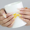 Hand holding a cup while wearing Naillover’s yellow and galaxy swirl stiletto nails with dimensional metallic details