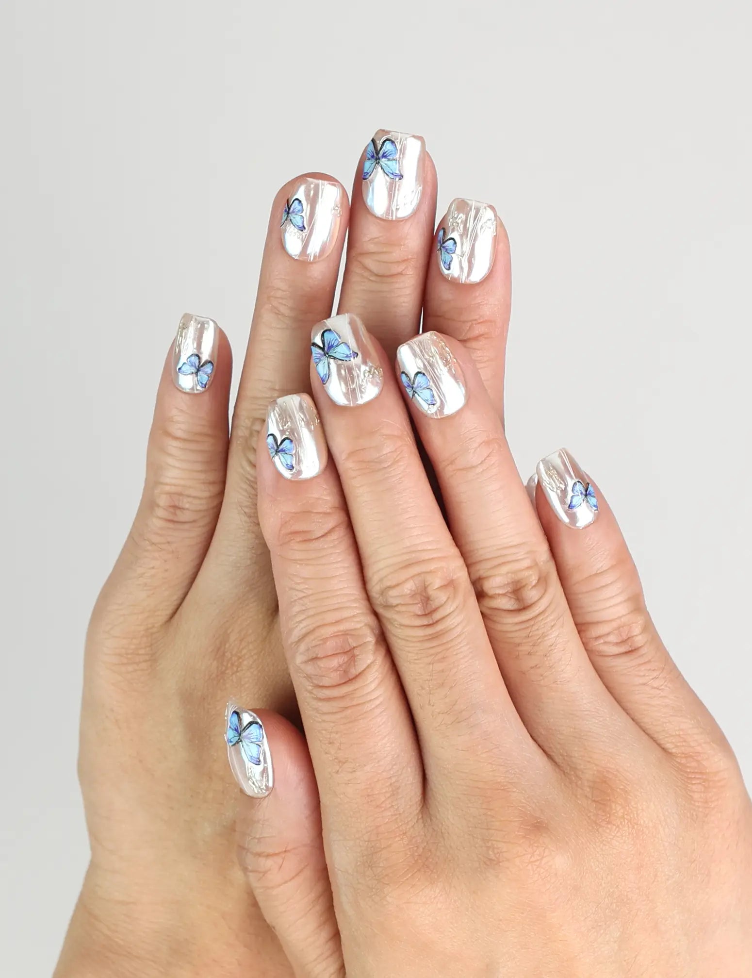 Hand wearing Butterfly Light short press-on nails with chrome base and blue butterflies from Naillover Singapore.