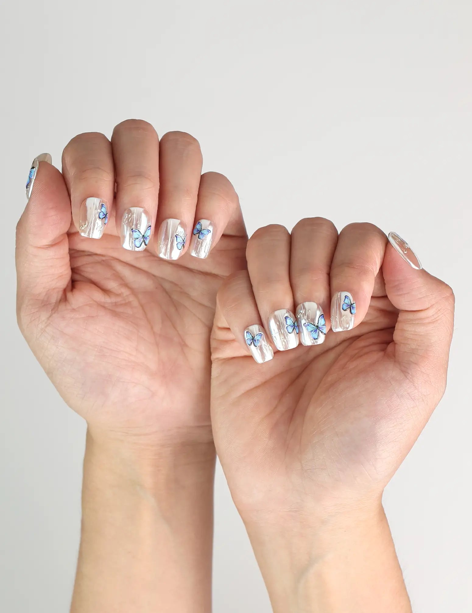 Butterfly Light handmade press-on nails in chrome with blue butterflies, worn for an elegant garden-inspired look in Singapore.