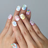 Hand model wearing short pastel press-on nails with 3D ice cream cones and gummy bear charms in pink and blue