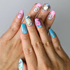 Hand model wearing short oval press-on nails with rainbow doodles, bright smiley faces, and playful patterns