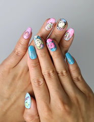 Hand model wearing short oval press-on nails with rainbow doodles, bright smiley faces, and playful patterns