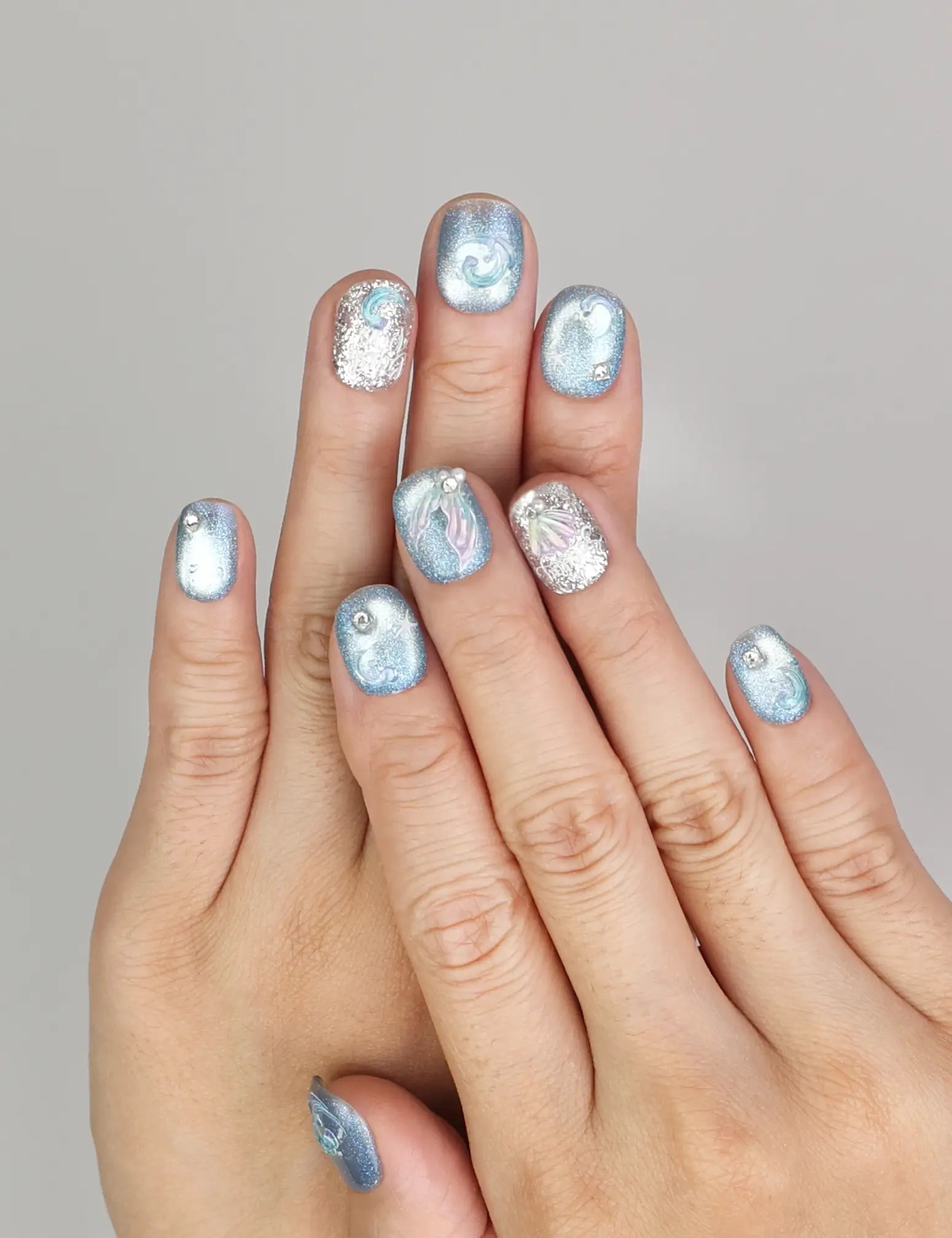 Hand wearing Naillover Celestial Blue handmade press on nails with shimmering blue swirls and glitter details.
