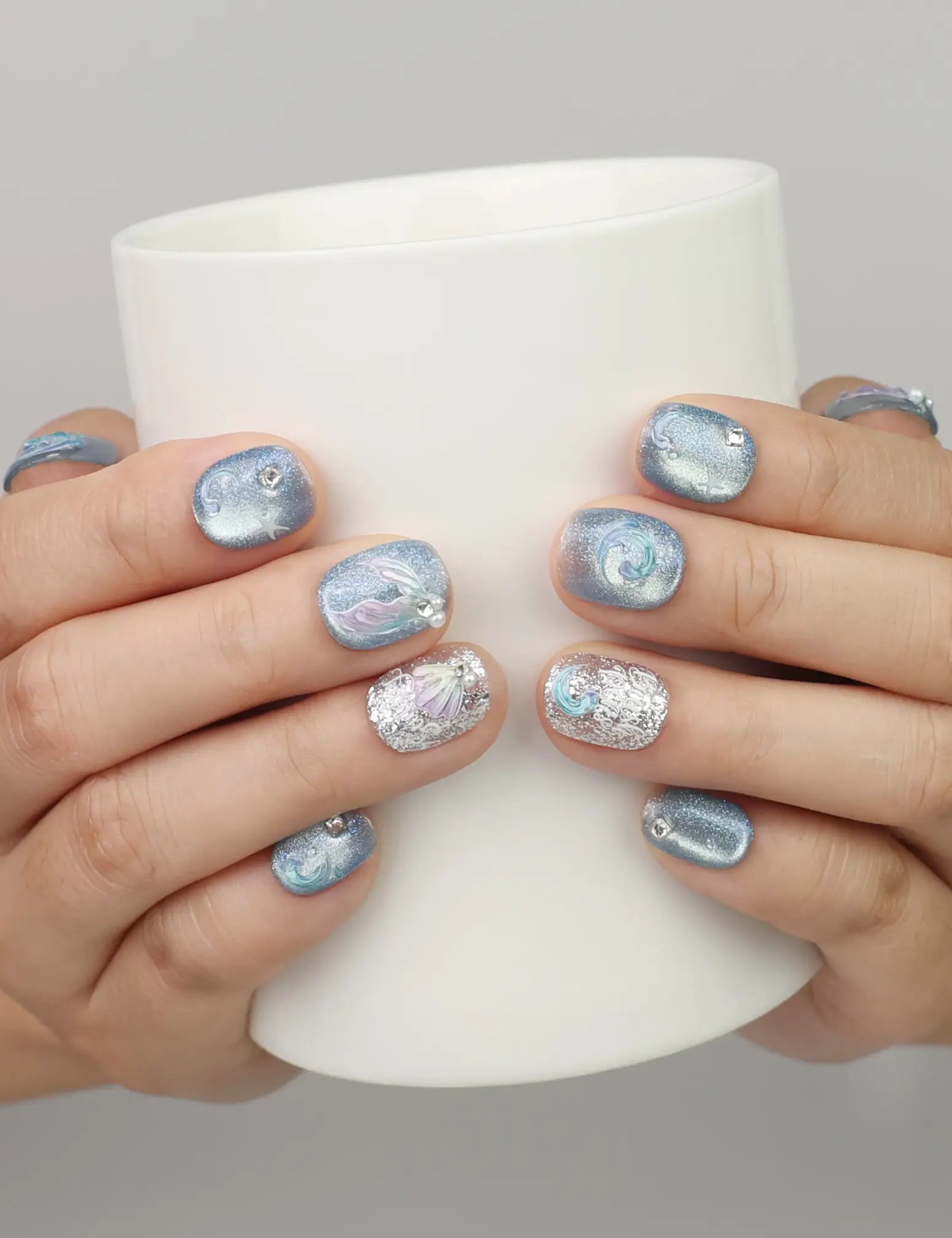 Hand holding a cup while wearing Naillover Celestial Blue Singapore press on nails with glitter and metallic patterns.