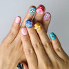 Hand model wearing short squoval press-on nails with playful 3D flowers, hearts, and multicolor googly eyes