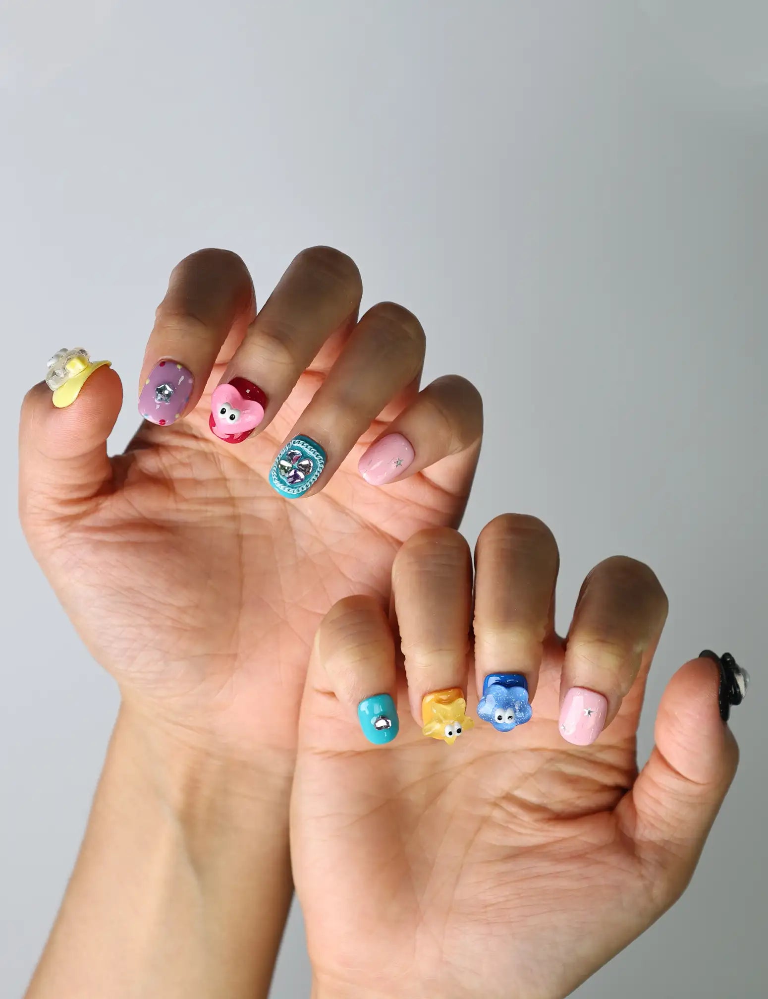 Cute and creative squoval nails with a glossy finish, combining handmade hearts, flowers, and googly elements