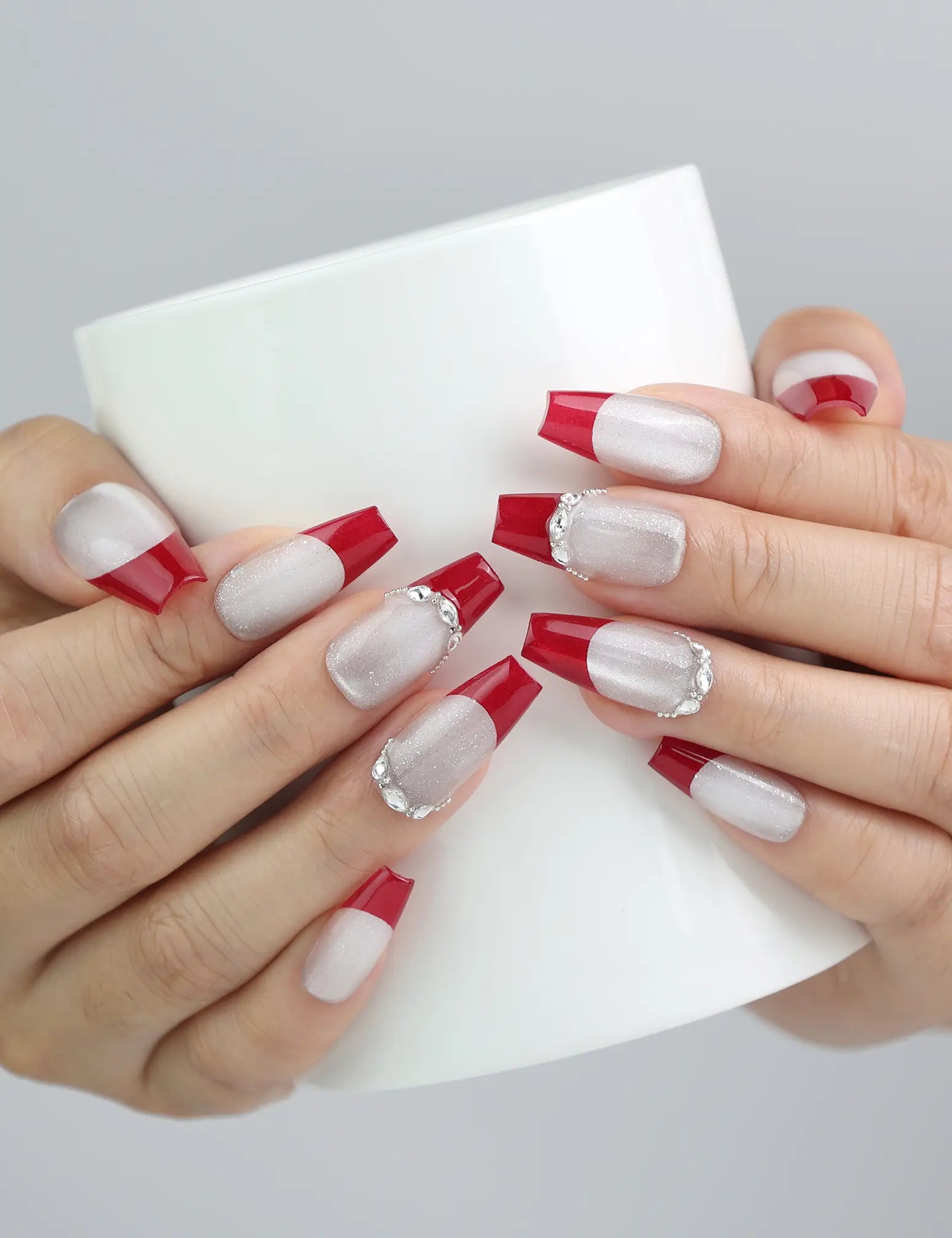 Hand holding a cup, showcasing Naillover’s crimson to silver glitter ombré coffin press-on nails in a glam style