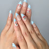Hand model wearing medium almond nails in soft blue with gingham French tips and tiny cherry embellishments
