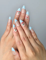 Hand model wearing medium almond nails in soft blue with gingham French tips and tiny cherry embellishments