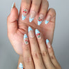 Close-up of handmade blue press-on nails featuring red cherry charms and pastel blue gingham patterns