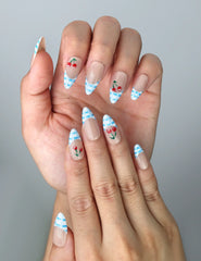 Close-up of handmade blue press-on nails featuring red cherry charms and pastel blue gingham patterns