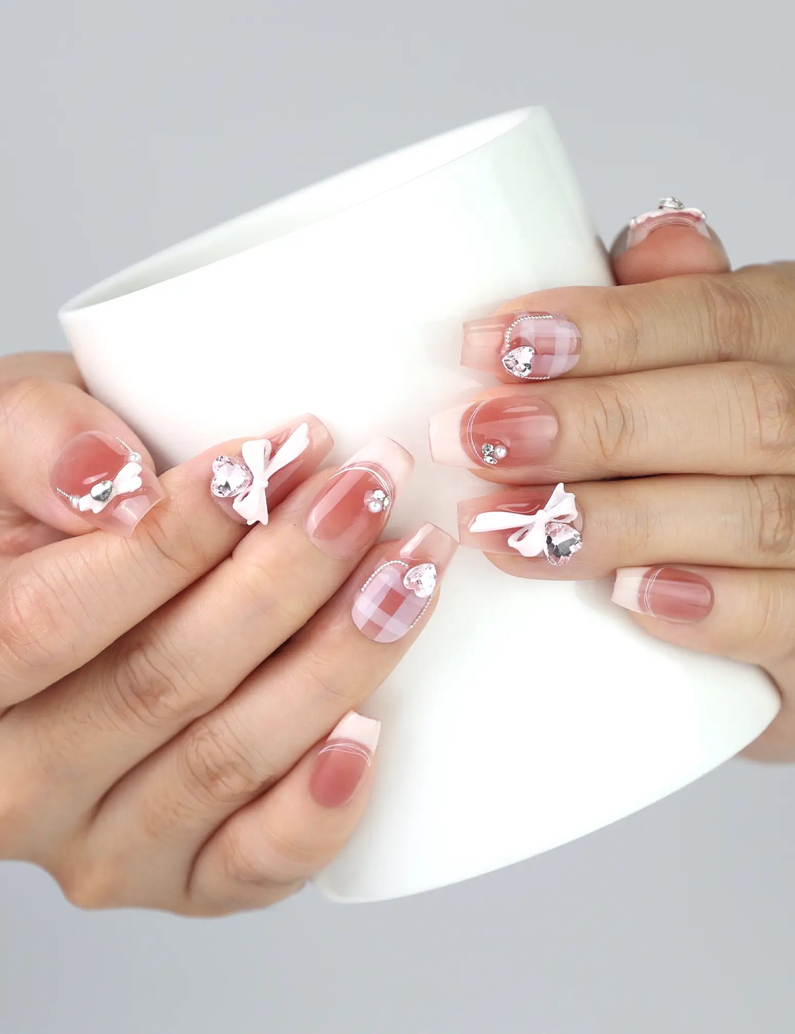 Hand holding a cup, showcasing Cherry Bow Crush handmade press on nails with 3D bows and rhinestones from naillover SG collection