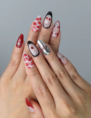 Hand model wearing medium almond red nails with 3D cherry lip art and cute pink bow accents