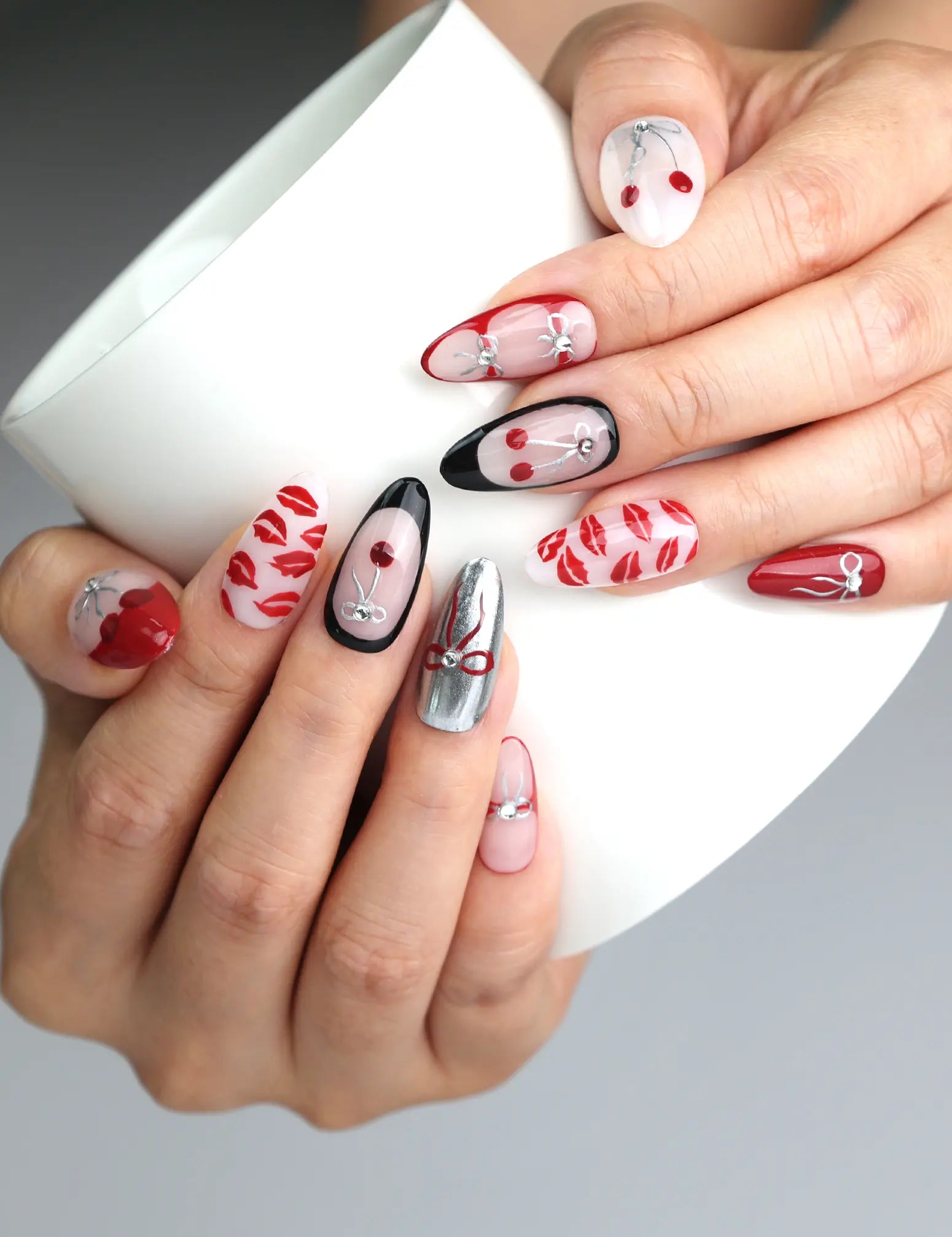 Hand holding a cup, showcasing Naillover’s red press-on nails with cherry lips and delicate bow accents